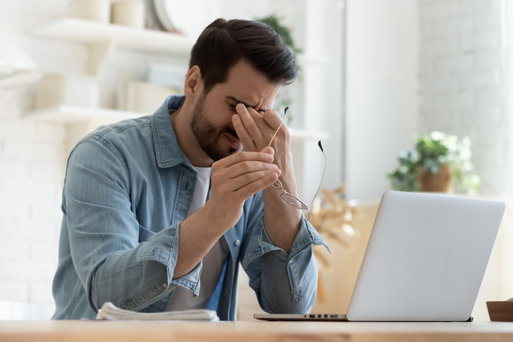 man tiredly rubbing his eyes in front of laptop