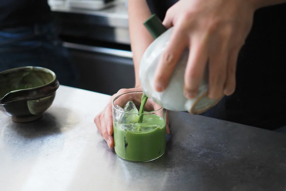 hands pouring green juice from bowl to cup